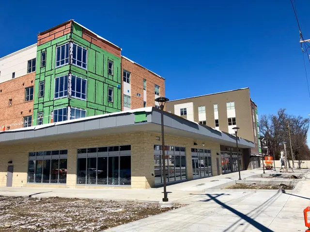 The image shows a large building with a lot of windows on the side of it, surrounded by street...