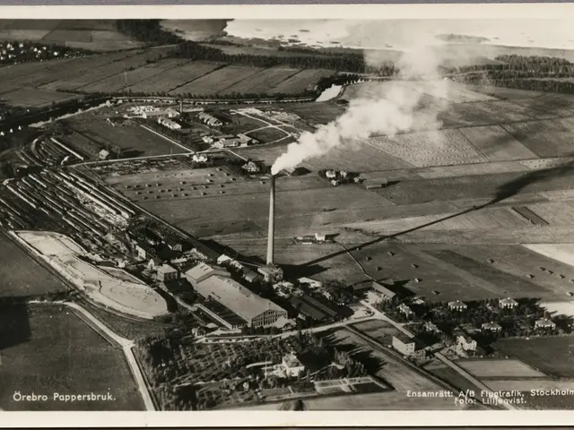 The image shows an aerial view of a factory with smoke billowing out of it, surrounded by...