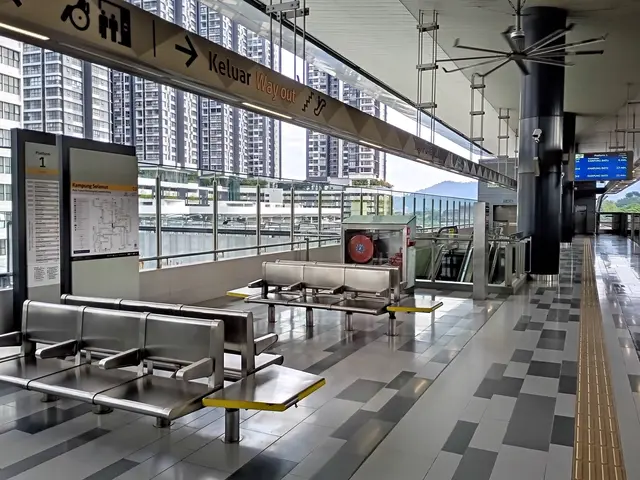 The image shows an empty waiting area in an airport with a lot of benches, boards with text printed...