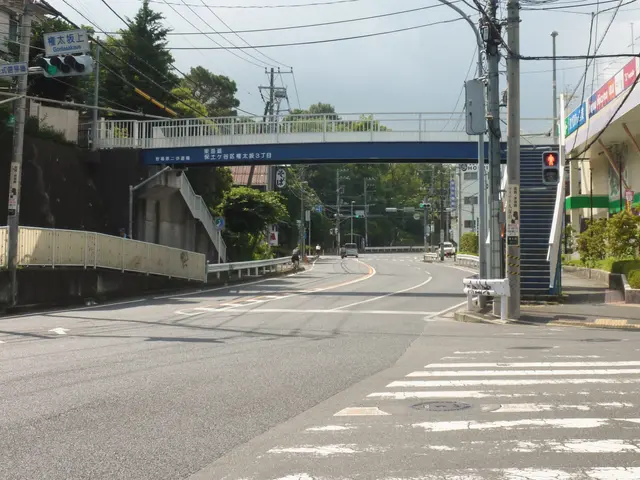 The image shows a city street with a pedestrian bridge over it. There are vehicles on the road,...