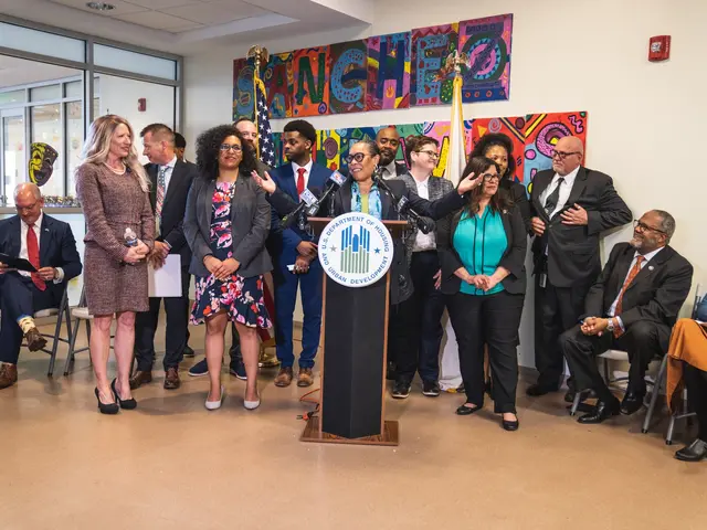 The image shows a group of people standing in front of a podium with a microphone and a board with...