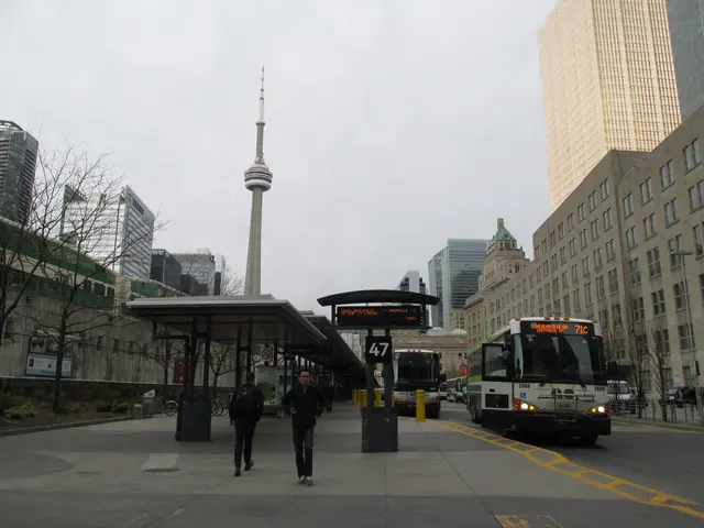The image shows a bustling city street with a bus stopped at a bus stop in front of a tall...