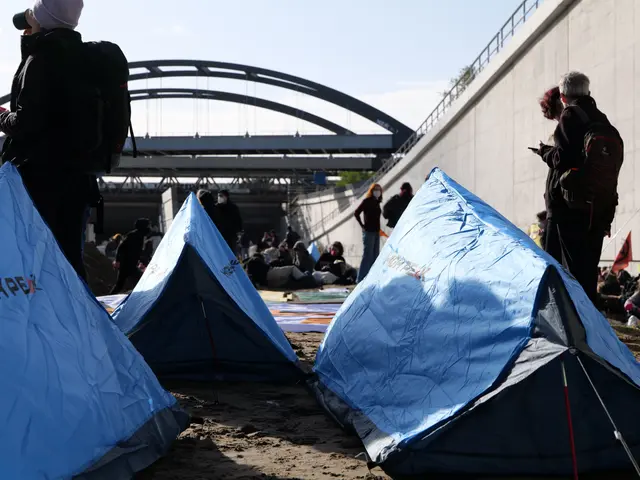 The image shows a group of people sitting on top of a sandy beach next to tents, with a wall on the...