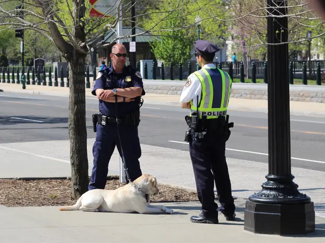 The image shows two police officers standing next to a dog on the sidewalk. The officer on the left...
