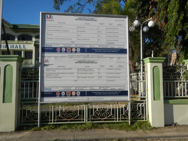 The image shows a sign on the side of a road in front of a building, surrounded by a metal fence, a...
