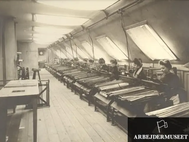 The image shows a black and white photo of a group of women working in a textile factory. They are...