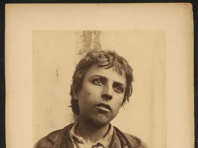 The image shows an old black and white photo of a young boy wearing a jacket. His face is clearly...