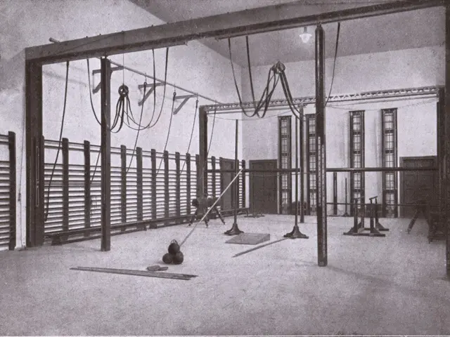 The image shows a black and white photo of a gym with a variety of equipment, including poles,...