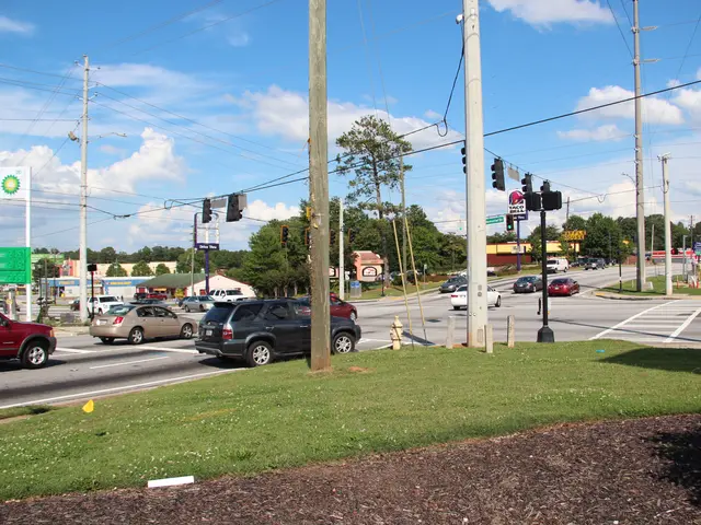 The image shows a city street with cars driving down it, electric poles with wires, traffic signals...