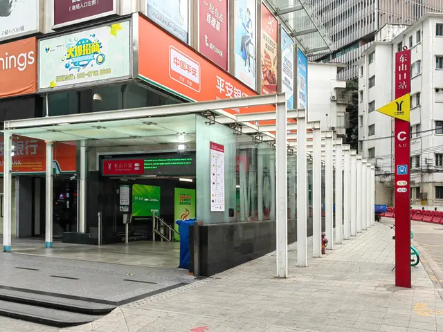 The image shows a bus stop on the side of a city street, with buildings on either side. At the...