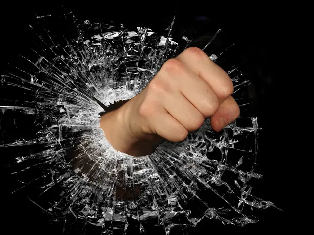 The image shows a person's hand breaking through a shattered glass window on a black background....