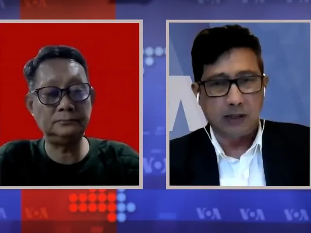 The image shows two men wearing glasses on a TV screen, with a blue and red background and white...