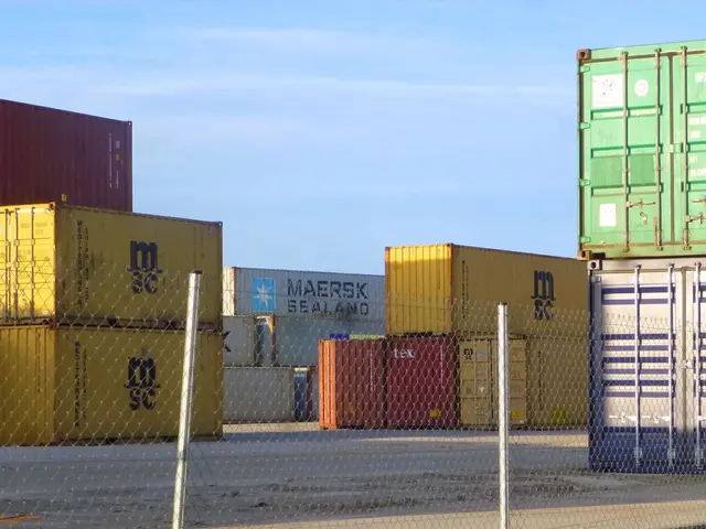 The image shows a large number of shipping containers stacked on top of each other, with a mesh...