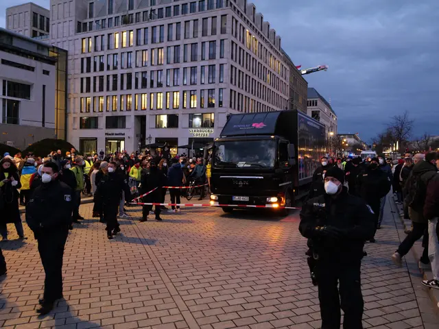 The image shows a group of people standing in front of a truck on a road surrounded by buildings...