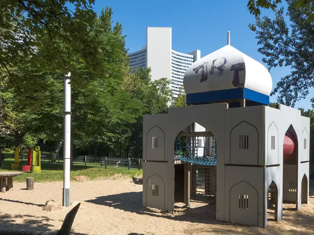 The image shows a playground with a play structure in the middle of it, surrounded by trees, poles,...
