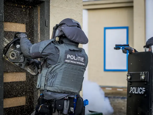 The image shows two police officers in riot gear standing in front of a building, with one of them...