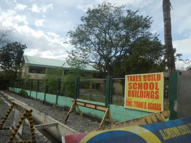The image shows a school building with a sign that reads "Taxes Build School Buildings" surrounded...