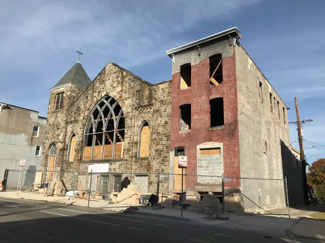 The image shows an old church with a steeple on the side of it, surrounded by buildings, trees,...