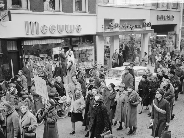 The image shows a crowd of people walking down a street in front of a store, with some of them...