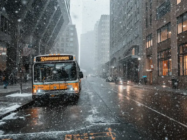 The image shows a yellow bus driving down a snowy city street, surrounded by tall buildings on...