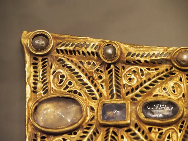 The image shows a close up of a gold pendant on display in a museum. The pendant is intricately...