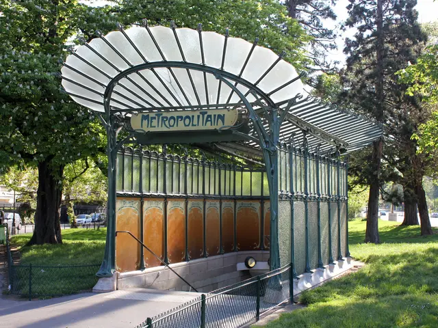 The image shows a bus stop in the middle of a park, surrounded by a metal fence, grass, a group of...