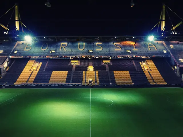 The image shows a soccer field at night with a lot of lights illuminating the stadium. The ground...