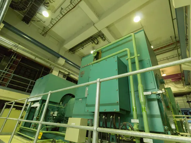 The image shows a large machine inside of a building, surrounded by railings, pipes, lights, and...