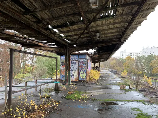 The image shows an abandoned train station with graffiti on the side of it. Underneath the bridge,...
