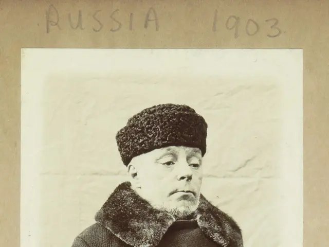 The image shows an old black and white photo of a man wearing a fur coat and a cap. The man is...