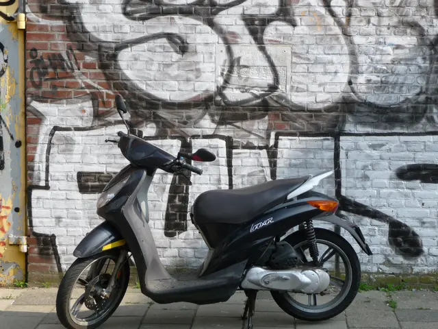 The image shows a motor scooter parked in front of a brick wall with graffiti on it. The scooter is...
