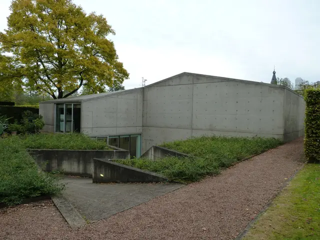 The image shows a concrete building with a walkway in front of it, surrounded by lush green grass...