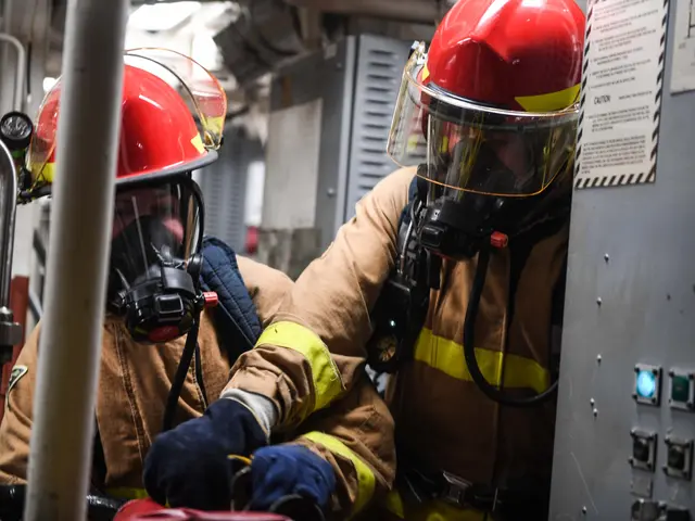 The image shows two firefighters in protective gear, wearing helmets and gas masks, working on a...