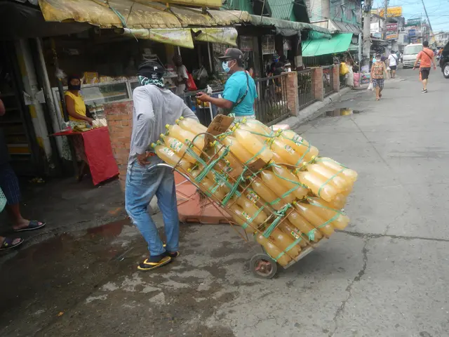 The image shows a man pushing a cart full of yellow cans down a street. He is wearing a blue...