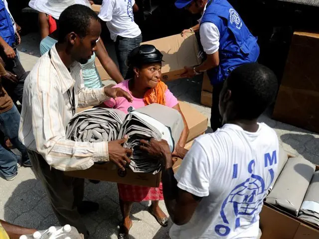 The image shows a group of people standing around a pile of boxes, with some of them holding...