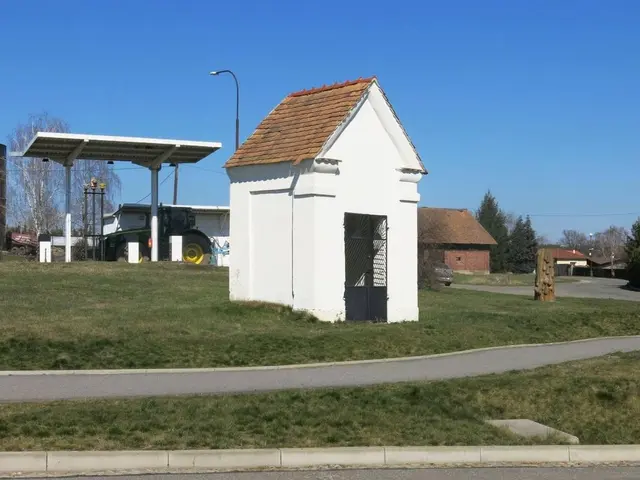 The image shows a small white building with a red roof sitting on the side of a road surrounded by...