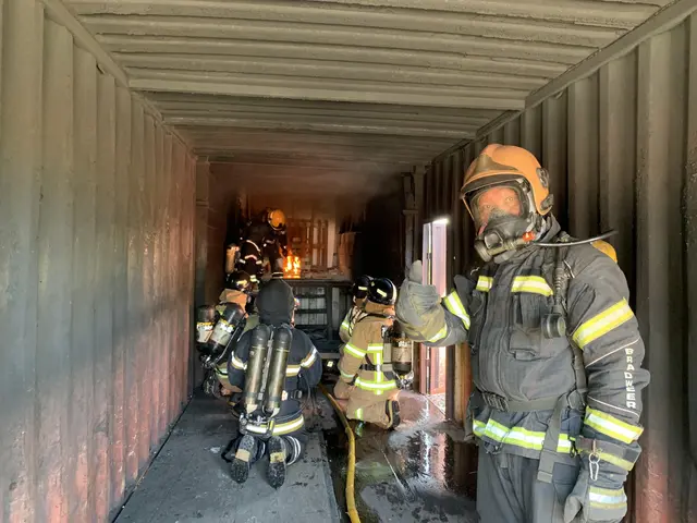 The image shows a group of firefighters in a shipping container, wearing helmets, gloves, and...