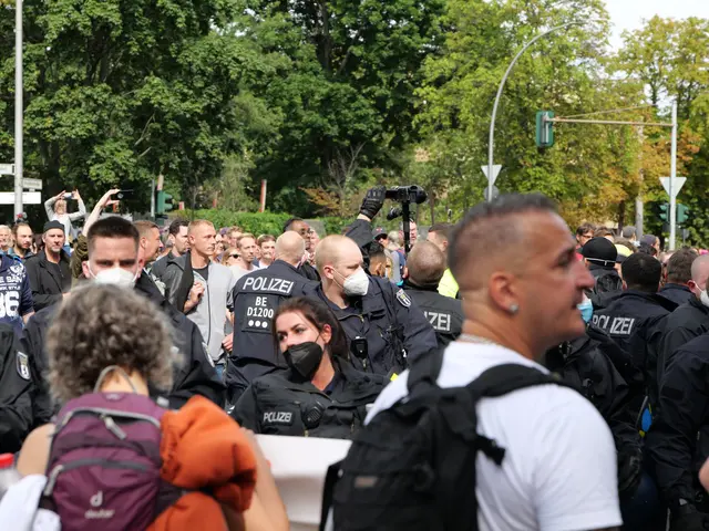 The image shows a large group of people standing in front of a crowd of police officers. Some of...