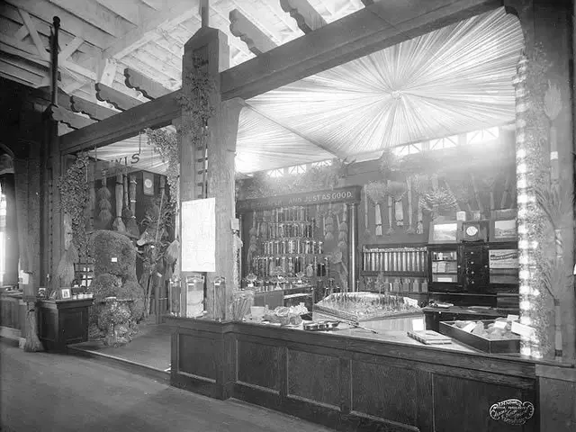 The image shows an old black and white photo of a store with a counter in the center. On the...