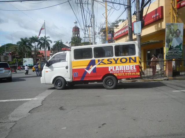 The image shows a white and red shuttle bus driving down a street lined with tall buildings. There...