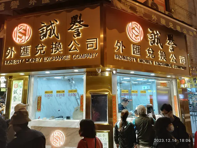The image shows a group of people standing outside of a building at night, illuminated by lights...