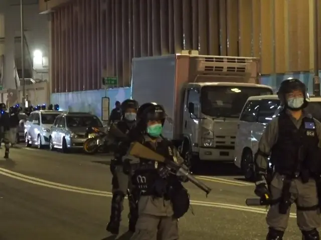 The image shows a group of police officers standing on the side of a street at night. They are...