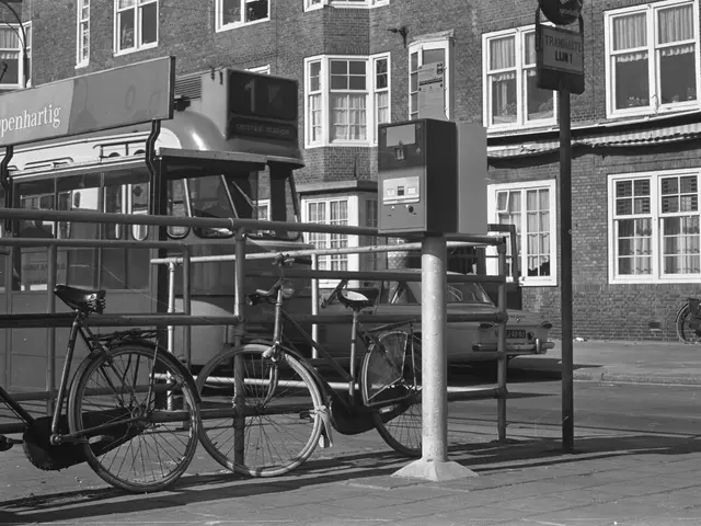 The image shows a black and white scene of a bus stop with bicycles parked on the side of the road....