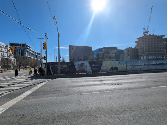 The image shows a city street with people crossing the street in front of a construction site....