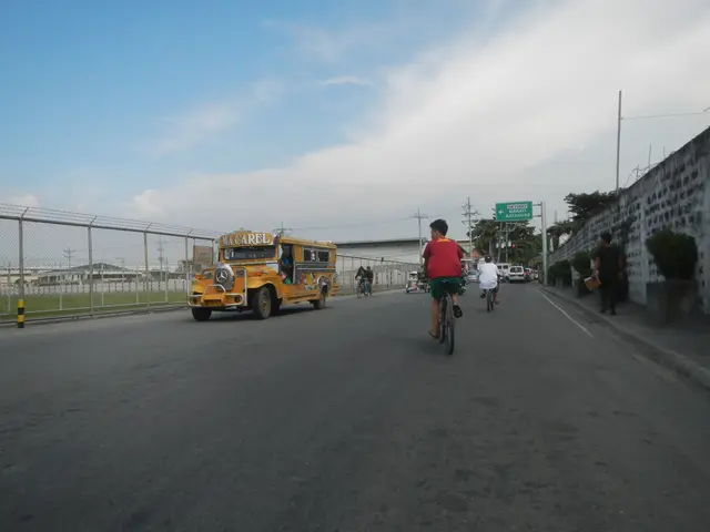 The image shows a group of people riding bicycles down a street next to a yellow school bus. On the...