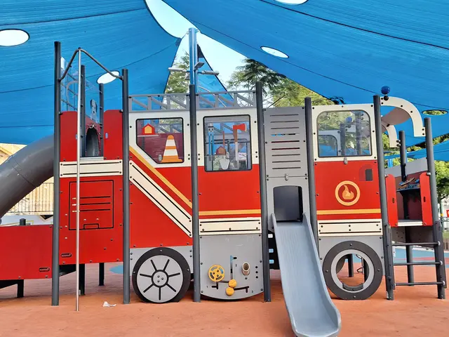 The image shows a playground with a fire truck-shaped play structure featuring a slide and a blue...