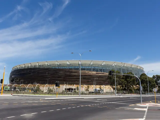 The image shows a large stadium with a lot of traffic in front of it, surrounded by street poles,...
