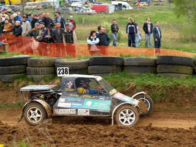 The image shows a man driving a buggy down a dirt road in front of a crowd of people, some of whom...