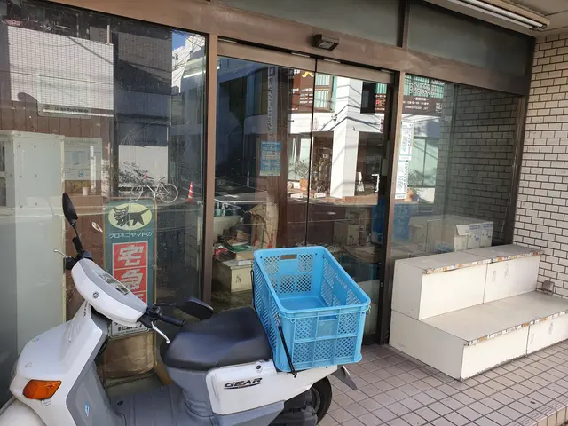 The image shows a scooter parked in front of a store with a blue basket on the back of it. The...