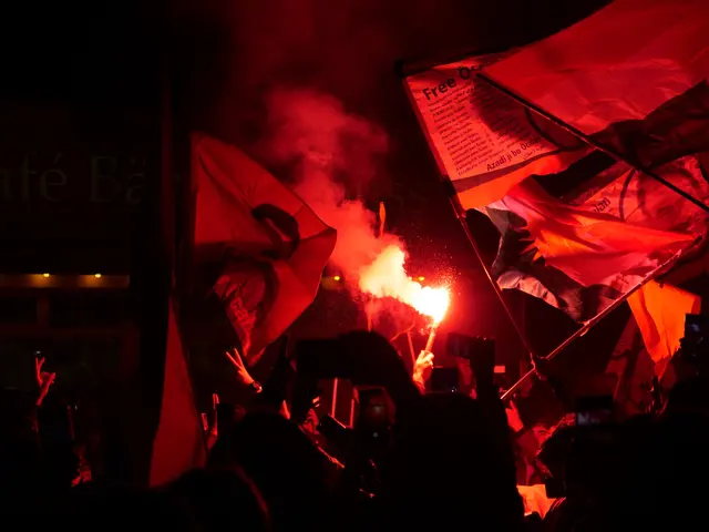 The image shows a group of people holding flags and flares in the air, illuminated by the light of...